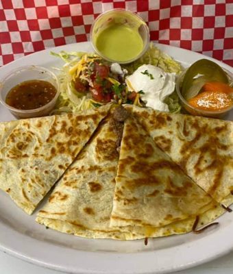 A plate of golden quesadillas served with a small bowl of dipping sauce.