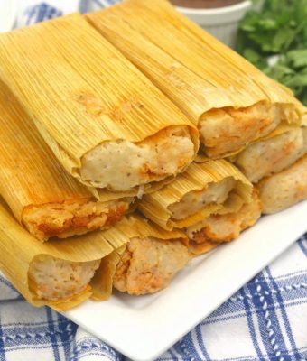 A plate of chicken tamales, wrapped in corn husks, garnished with salsa and fresh cilantro.