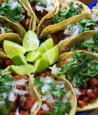 A plate of tacos filled with seasoned meat, fresh lettuce, and lime wedges for garnish.