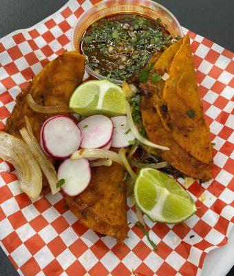 A plate featuring a tortilla, sliced onion, and a small bowl of salsa on the side.