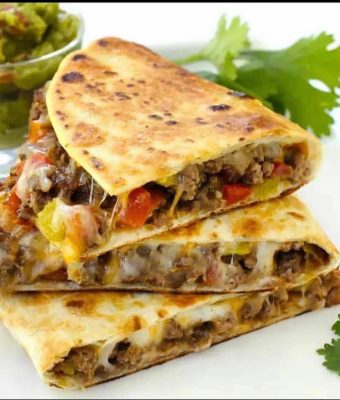 A stack of quesadillas filled with meat and vegetables, served on a white plate.